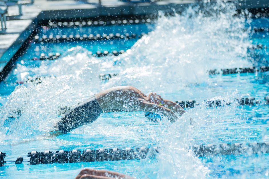 Dynamic shot of a swimmer diving into the pool during a competitive swim meet, creating a large splash.
